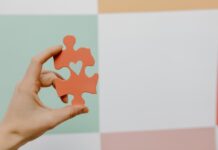 Amar o Próximo: Descubra o poder transformador deste ato Close-up of a hand holding a heart-shaped puzzle piece against a colorful background.