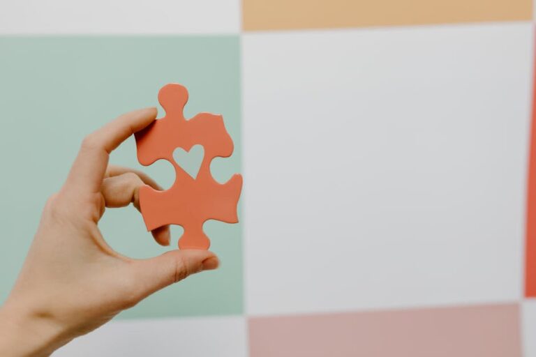 Close-up of a hand holding a heart-shaped puzzle piece against a colorful background.
