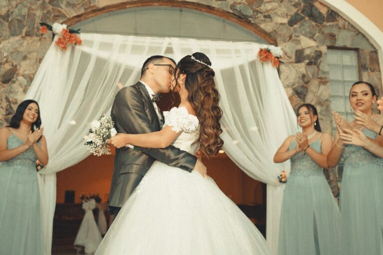 A joyful wedding moment capturing the bride and groom sharing a kiss surrounded by bridesmaids.