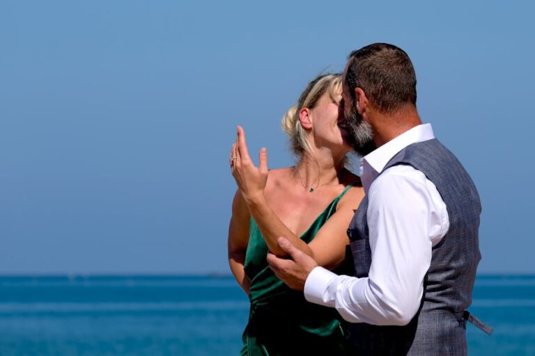A couple sharing an intimate moment at the beach with a clear blue ocean backdrop.