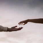 Two hands reaching towards each other against a soft twilight sky symbolizing connection and love.