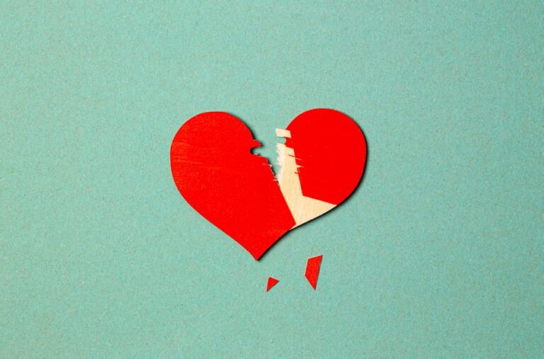 A torn red paper heart on a blue background symbolizes broken love or heartache.