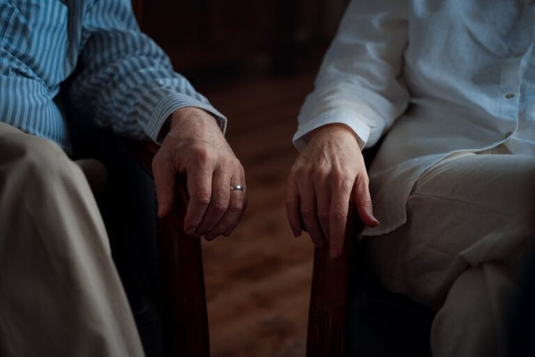 A touching moment capturing an elderly couple's hands resting on armchairs indoors.