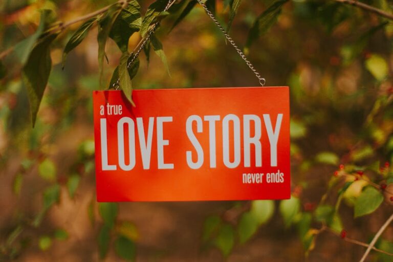 Orange sign stating 'A true love story never ends' hanging from a tree branch outdoors.