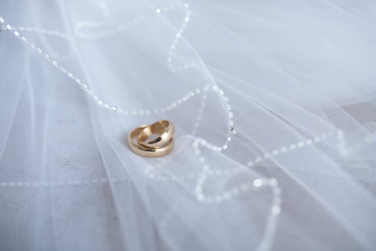 Beautiful gold wedding rings resting on soft white tulle with delicate beaded details, symbolizing love and commitment.