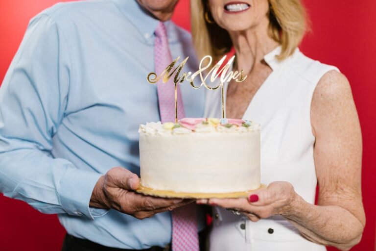 An elderly couple joyfully holding a 'Mr & Mrs' wedding anniversary cake.