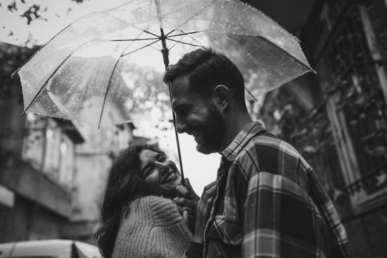 Happy couple sharing an umbrella, smiling in a rainy street, exuding romance and joy.
